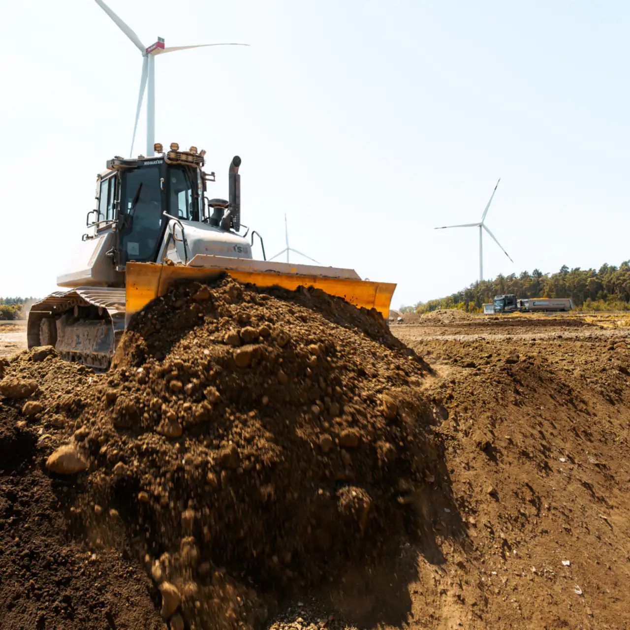 Planierraupe schiebt Boden in der Sandgrube, im Hintergrund Windräder